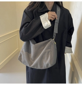 Detailed view of grey suede baguette bag with wide strap and golden hardware on model