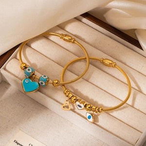 Detail of 18K gold-plated cable bangles with blue heart and evil eye enamel charms
