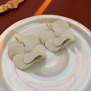Detailed macro view of petal-shaped earrings in Morandi green on a glossy ceramic plate