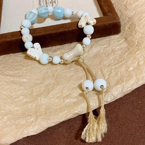 Detail of handmade ceramic bracelet with blue marble beads, butterfly charm and hemp tassel