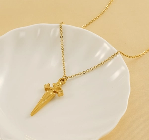 Detailed close-up of a golden cross sword pendant resting on a white shell tray