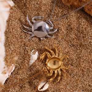 Detailed beach scene of gold and silver crab pendant necklaces on sand with sea shells