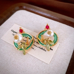 Gros plan de boucles d'oreilles vintage en or avec émail vert, perles et pierres rouges