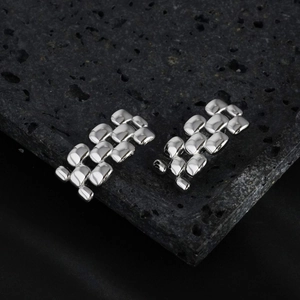 Silver geometric link earrings with watch strap design on black volcanic rock background