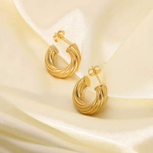 Detailed close-up of 18K gold plated twisted C-shape hoop earrings on yellow silk fabric