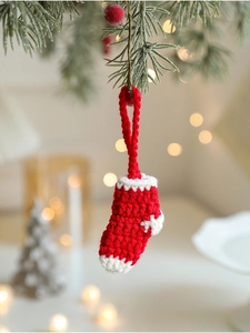 Close-up of handmade crochet Christmas stocking ornament hanging on a pine branch with bokeh