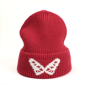 Detail of dark red knit beanie showing white butterfly jacquard pattern on ribbed cuff