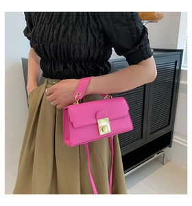 Detail of rose pink handbag with gold buckle shown on model in a modern indoor setting