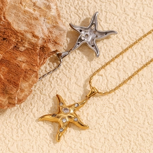 Detail of 18K gold starfish pendants with zircons and beaded chain on natural rock