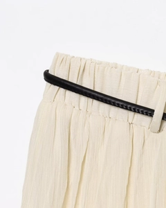 Détail macro de la taille d'une jupe midi plissée crème avec ceinture fine noire stylée