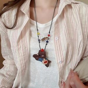 Detail shot of cute plush brown bear pendant with blue overalls and colorful beads on a cord
