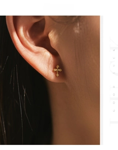 Close-up of woman wearing a minimalist gold cross stud earring with beaded relief detail