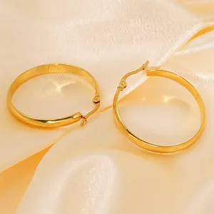 Polished gold round hoop earrings with secure clasp closure on elegant silk background