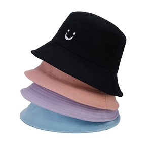 Detail of stacked cotton bucket hats in multiple colors featuring a white smiley embroidery