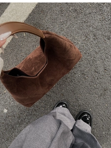Detail of dark brown matte suede hobo bag texture and leather strap held by a person