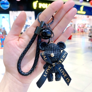 Detail of black woven bear keychain with metal whistle and gold lettered ribbon