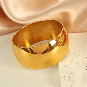 Polished wide 18K gold plated stainless steel bangle on stone and silk background