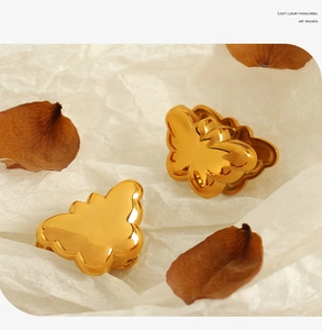 Artistic close-up of golden butterfly heart earrings with decorative dry petals on paper