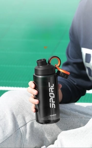 Person holding a smoke grey 800ml sports water bottle against a green stadium background