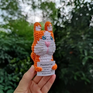 Nahaufnahme einer handgehaltenen gestrickten Katze mit einer ermutigenden Botschaftskarte