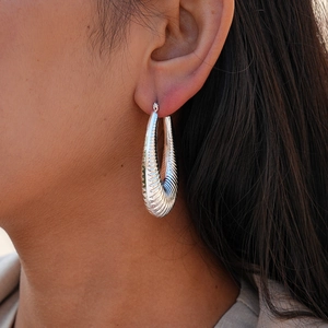Close-up of silver U-shaped earrings with horizontal ridge texture worn on a model
