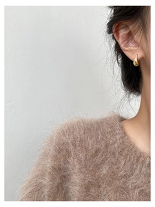 Close-up of golden teardrop earring with mirrored finish on a model's ear detail