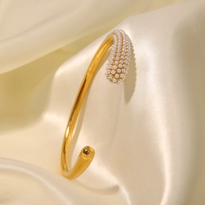 Detail of 18K gold-plated open cuff bracelet with white pearls on beige silk fabric