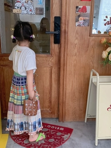 Outdoor back view of a child wearing a colorful patchwork plaid dress and woven bag