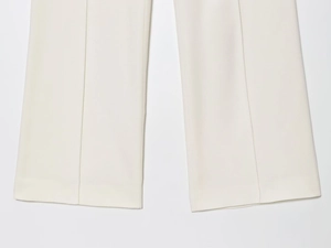 Detail der cremeweißen Hose mit weitem Bein, Bügelfalte und hochwertiger Stoffstruktur