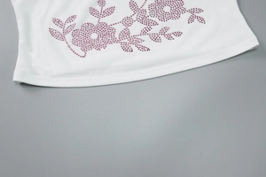 Close-up of white knitted top detail with purple and pink rhinestone flower pattern