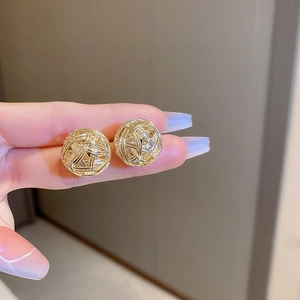 Close-up of golden woven texture round stud earrings with metallic thread detail