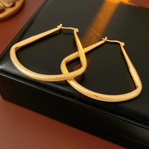 Vue détaillée des boucles d'oreilles créoles dorées mates sur une base en cuir noir