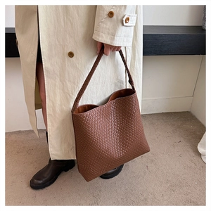 Close-up of brown woven leather large shoulder bag held by model in stylish beige coat