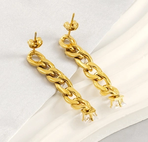 Close-up of gold chain earrings with a square zirconia drop on a white silk background