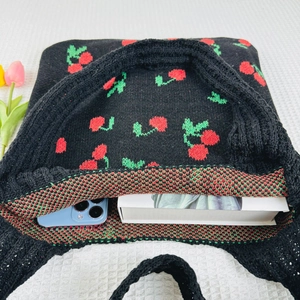 Top view of black knitted tote with cherry patterns, featuring phone and book inside