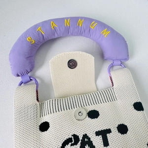 Close-up of knit tote bag showing metal magnetic closure and purple embroidered handle