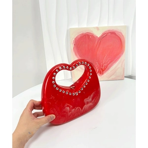 Close-up of red heart-shaped acrylic bag with marble texture and rhinestone handle