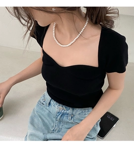 Détail d'un collier de perles blanches rondes porté avec un haut en tricot noir à col carré