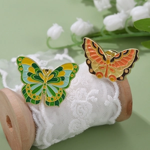 Colorful butterfly enamel pins in green and orange tones on a vintage wooden spool