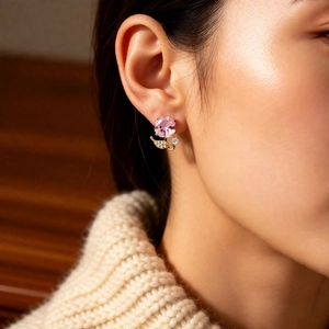 Gros plan de boucles d'oreilles fleurs plaquées or avec zircon rose sur mannequin en pull
