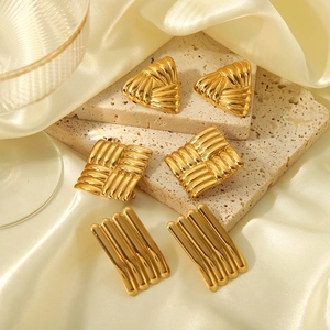 Detail von geometrischen Goldohrringen mit Streifenrelief auf Marmor und Seide