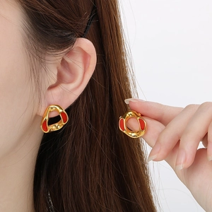Macro detail of geometric gold earrings with vibrant red enamel and sparkling inlay
