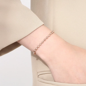 Close-up of a stylish rose gold bead chain bracelet worn on a wrist with a beige suit