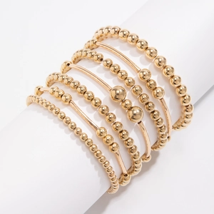 Detail of layered gold beaded bracelets with heart pendant on a white pedestal