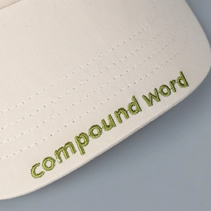 Primer plano del bordado verde 'compound word' en la visera de una gorra beige