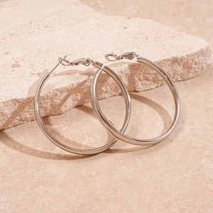 Close-up of large silver hoop earrings with a polished mirror finish on a textured stone