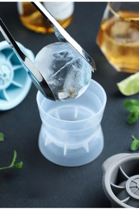 Macro shot of stainless steel tongs holding a large ice sphere over silicone molds