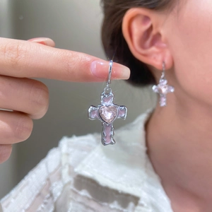 Close-up of silver cross earrings with pink heart crystal worn by a model