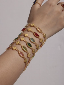 Close-up of layered gold bracelets with colorful marquise stones and heart charms on wrist