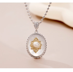 Macro shot of oval mother of pearl pendant with golden flower and pearl detail on bead chain